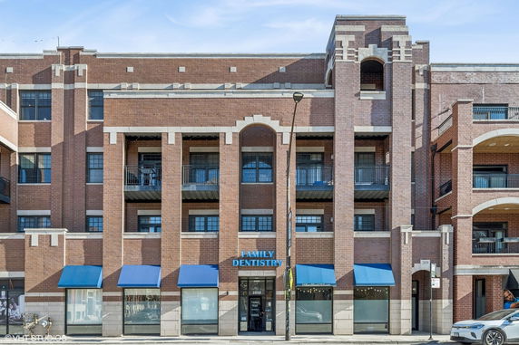 Front view of a multi-story brick building with balconies and blue awnings.