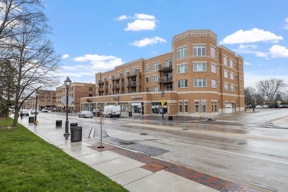 Front view of a multi-story brick building with balconies and retail stores on the ground floor.
