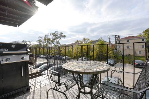 View from a balcony with outdoor furniture and a barbecue grill overlooking a parking area and trees.