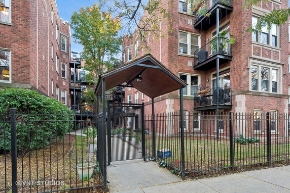 Front view of a multi-story brick apartment building with balconies and a gated entrance.