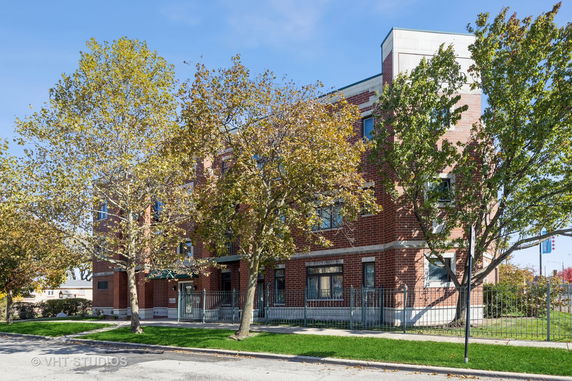 Front view of a multi-story brick building with trees and a fenced yard.