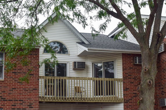 Front view of a house with brick and siding exterior featuring a small balcony and arched window.