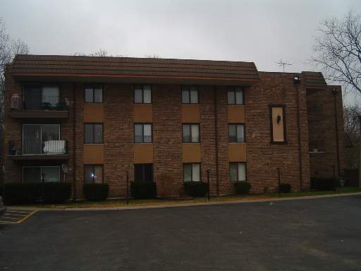 Front view of a three-story apartment building with a brown facade and multiple windows.