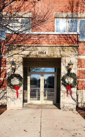 Front entrance of a brick building with holiday wreaths and double glass doors.