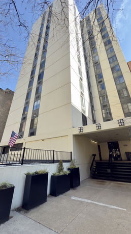 Front view of a multi-story residential building with an entrance and American flag.