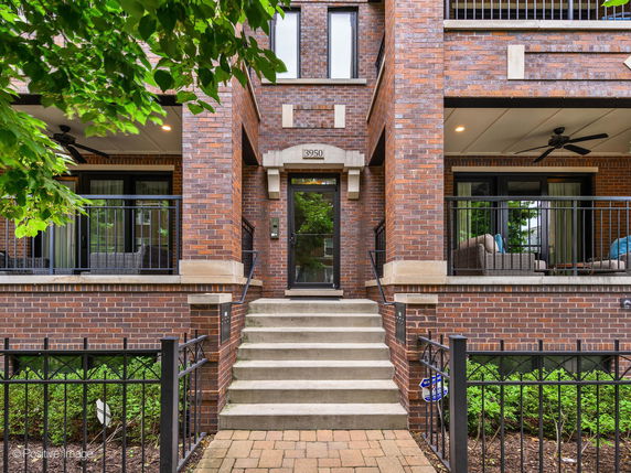 Front view of a multi-story brick building with a balcony and steps leading to the entrance.