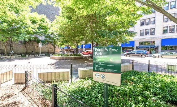 View of Printer's Row Park with surrounding buildings and parked cars.