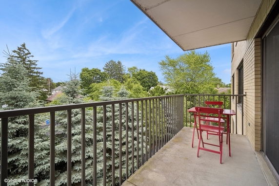 Balcony with red table and chairs, surrounded by trees, offering a view of the outdoors.