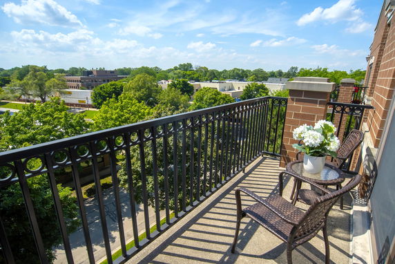 View from a balcony with chairs and a table, overlooking a green area and surrounding buildings.