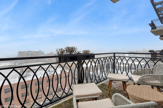 Balcony view overlooking surrounding buildings with patio furniture and a railing.