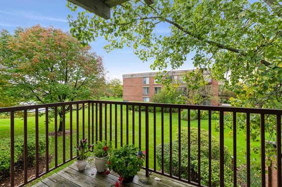 View from a balcony overlooking a grassy area with trees and a three-story brick building.