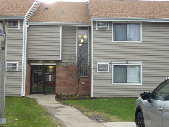 Front view of a two-story building with tan siding and a sloped roof.
