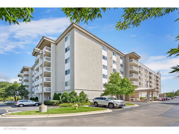 Front view of a multi-story apartment building with balconies and a parking area.