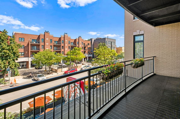 Panoramic view from a balcony showing a tree-lined street and brick buildings.