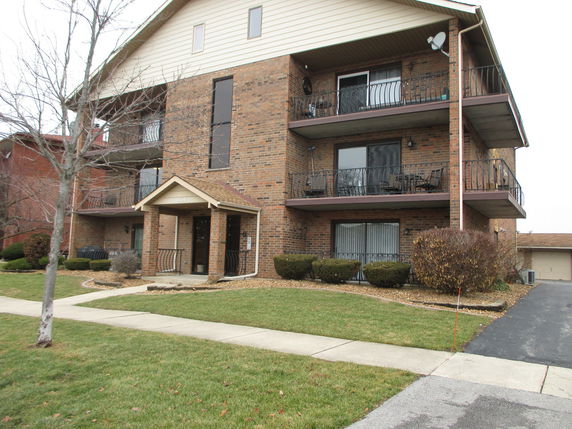 Front view of a three-story brick apartment building with balconies.