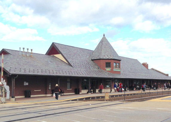 Front view of a brick building with a conical roof section and a train platform in front.