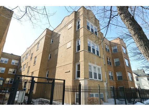 Front view of a multi-story brick apartment building with multiple windows and a metal fence.