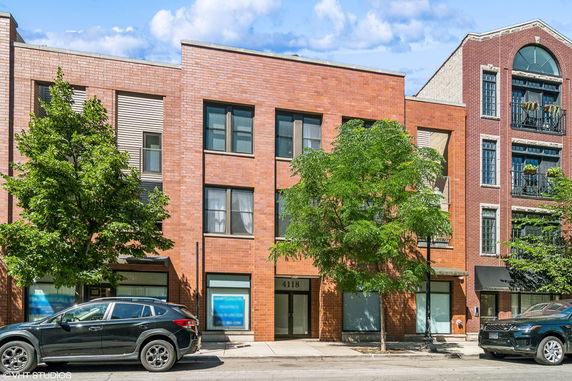 Front view of a three-story brick building with multiple windows and trees in front.