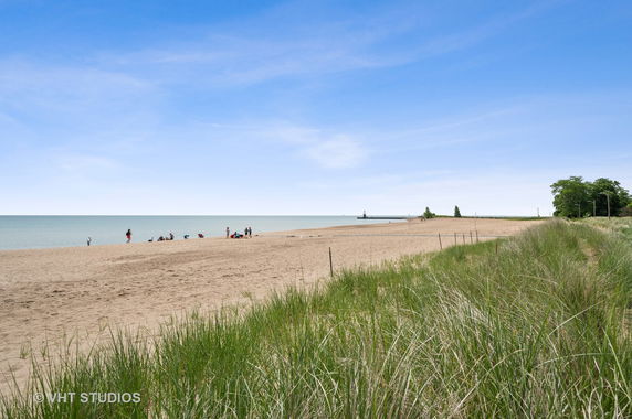 View of a sandy beach with grassy dunes and people in the distance.