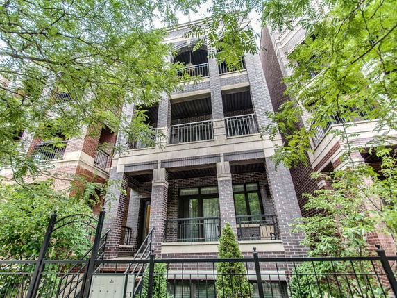 Front view of a multi-story brick building with balconies and a gated entrance.