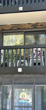 View of a building with a balcony featuring potted plants and chairs visible through a wooden railing.