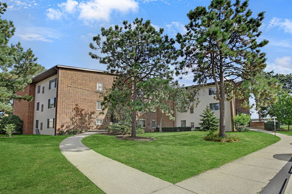 Front view of a multi-story brick apartment building with pathways and trees.