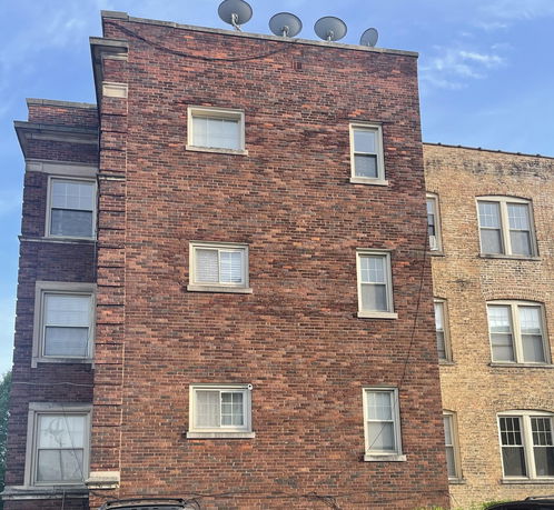 Side view of a brick residential building with multiple satellite dishes on the roof.