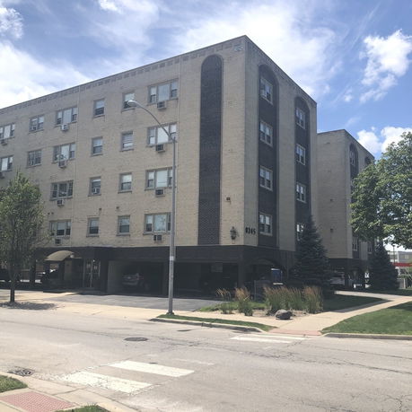 Front view of a multi-story apartment building with multiple windows and a parking area underneath.