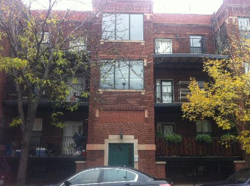 Front view of a three-story brick apartment building with balconies.