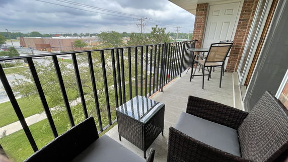 View from a balcony with chairs and table, overlooking buildings and trees.