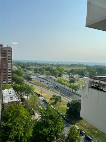 Elevated view overlooking a road with vehicles, trees, and a body of water in the background.