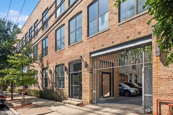 Front view of a brick apartment building with large windows and an entrance gate.