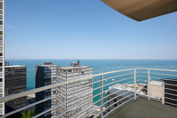 Panoramic view from a high-rise building balcony overlooking the ocean and nearby buildings.