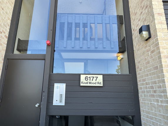 Front view of a building entrance with a glass facade and the address 6177 Knoll Wood Rd.