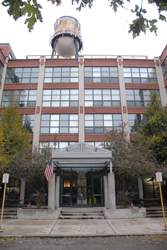 Front view of a multi-story brick building with large windows and a water tower on the roof.