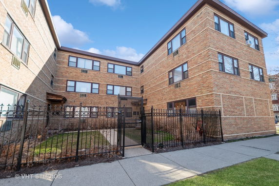 Front view of a multi-story brick apartment building with a fenced entrance.
