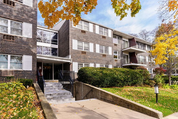 Front view of a multi-story brick apartment building with balconies and an entrance staircase.
