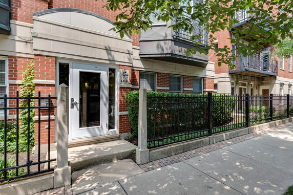 Front view of a brick residential building with a black metal fence and shrubs.