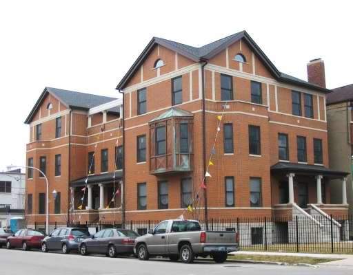 Front view of a multi-story brick building with multiple gabled roofs and a bay window.