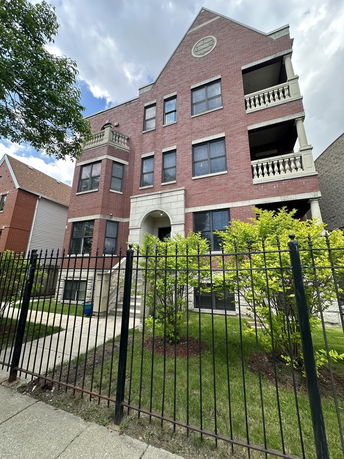 Front view of a multi-story brick building with balconies and a fenced yard.