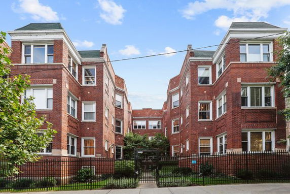 Front view of a brick residential building with multiple stories and a gated entrance.