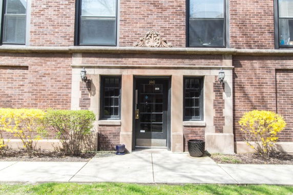 Front view of a brick building with a central entrance door and decorative trim.