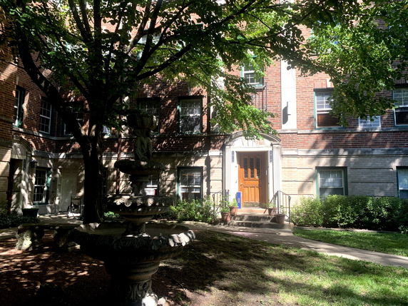 Front view of a brick building with a central entrance and windows bordered by greenery.