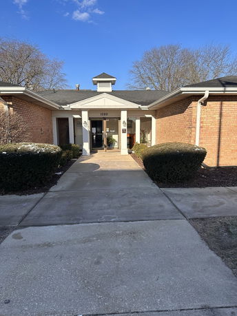 Front view of a brick building with a central entrance and a small roof structure.