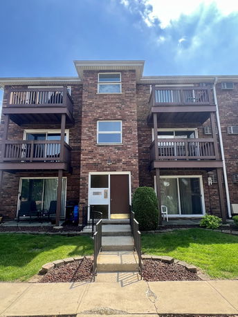 Front view of a three-story brick apartment building with balconies.