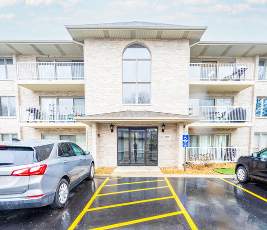Front view of a multi-story apartment building with balconies and parking area.