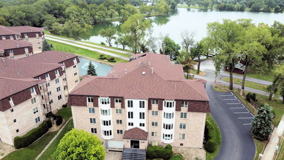 Aerial view of a multi-story apartment complex with red roofs, surrounded by trees and a large body of water.