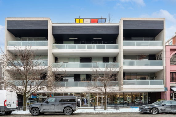Front view of a modern multi-story building with glass balconies and a colorful rooftop feature.