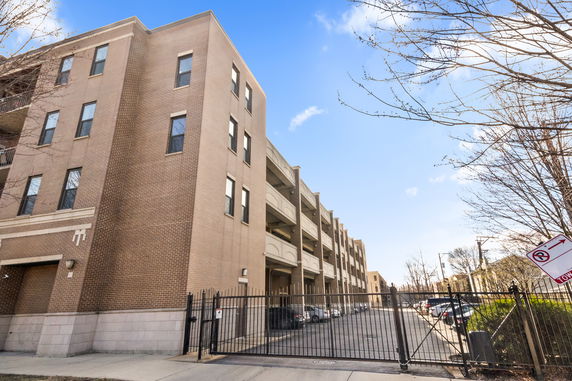 Front view of a multi-story brick building with gated entry and adjacent parking area.