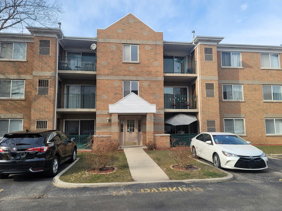 Front view of a three-story brick apartment building with balconies.